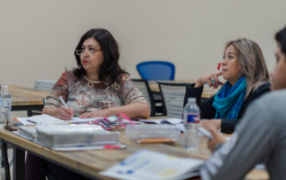 Adult students reviewing study materials and binders together during an ESL to GED class session
