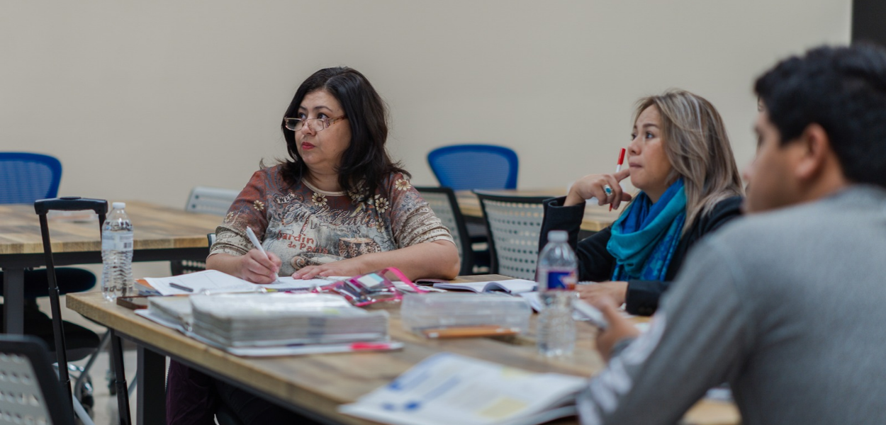 Adult students reviewing study materials and binders together during an ESL to GED class session